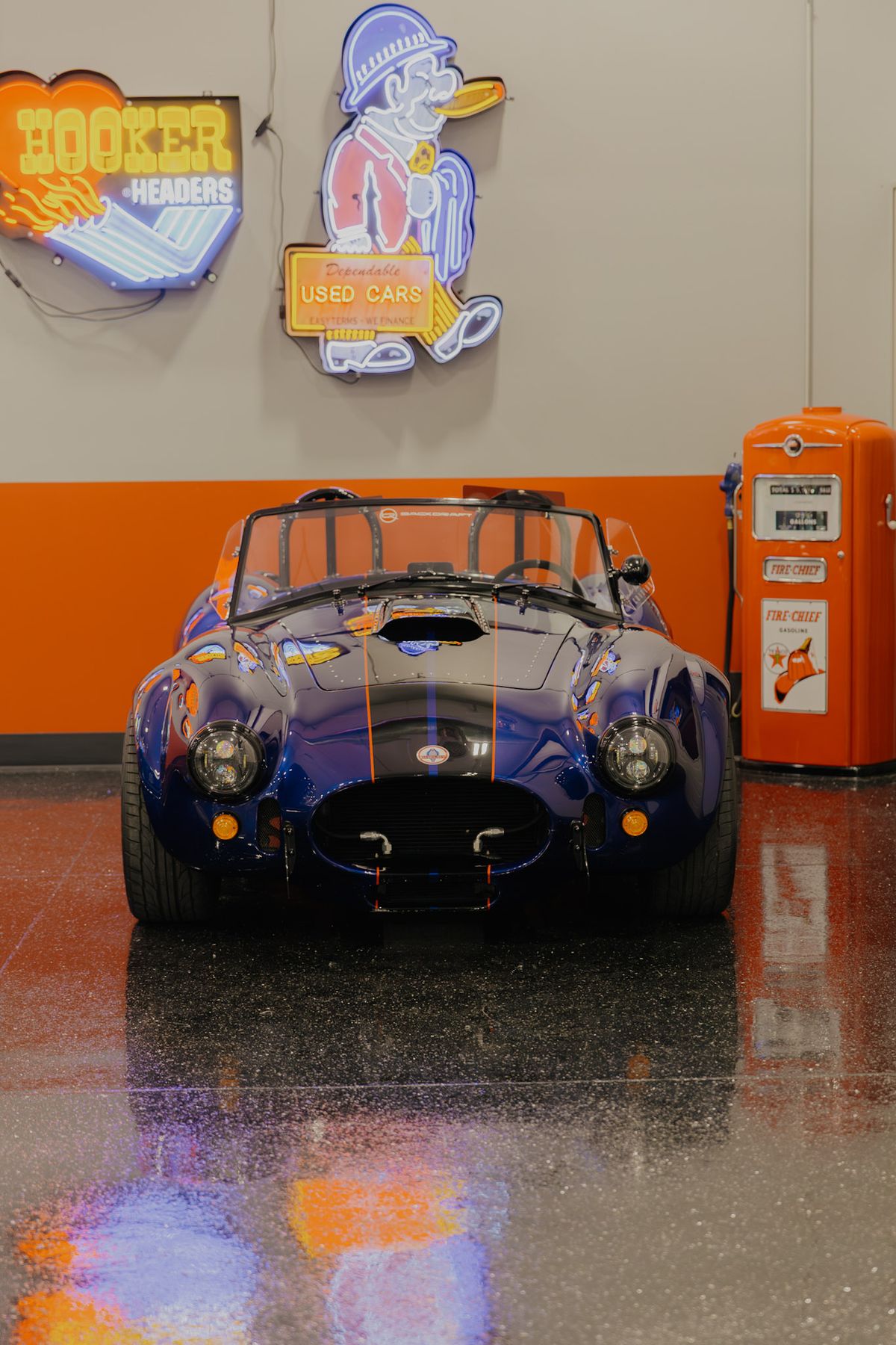 Deep blue Cobra roadster head on in the showroom