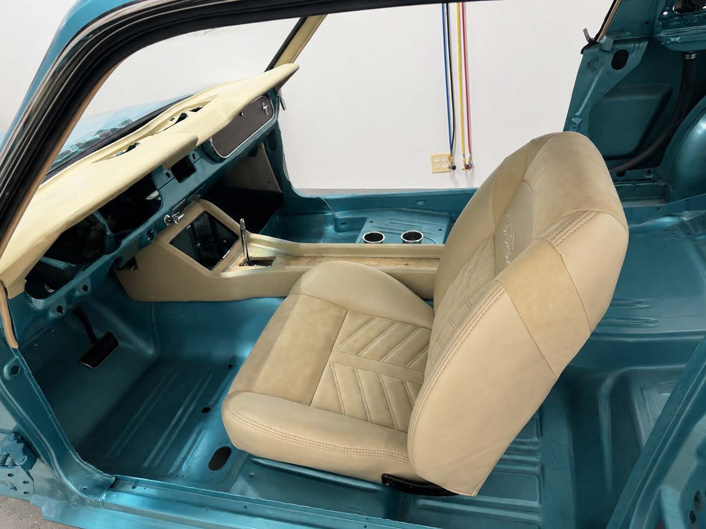 Cream stitched seats and custom console taking shape inside a teal Mustang